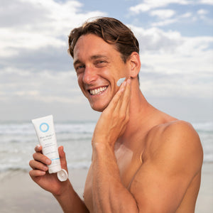 Ali Day Surf Ironman Champion of 2022 applying  Blue Healer cream to his face while standing at the beach.